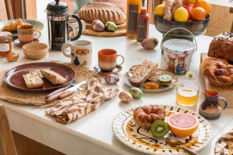Table de petit-déjeuner abondante avec pains et viennoiseries, tasses de café, confitures, jus d’orange et fruits frais, décorée d’œufs colorés évoquant une ambiance de brunch de Pâques lumineux et convivial.